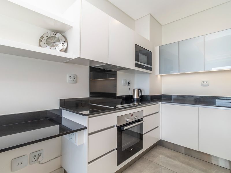 Modern kitchen featuring sleek white cabinetry, contrasting black granite countertops, integrated appliances, and high-quality tiled flooring.