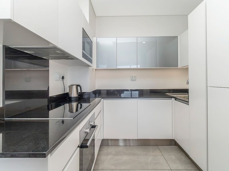 Modern kitchen featuring sleek white cabinetry, contrasting black stone countertops, integrated appliances, and high-quality tiled flooring.