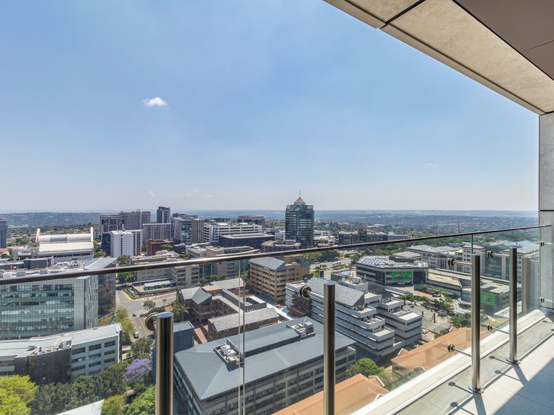 A modern high-rise balcony featuring a sleek glass balustrade and stainless steel handrail, offering expansive panoramic views of the surrounding city skyline.