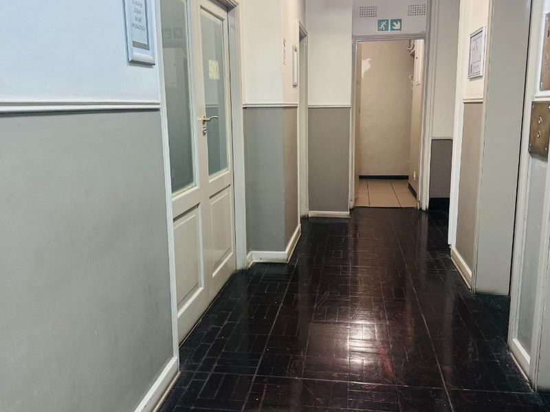 A functional office hallway featuring dark parquet flooring, emergency exit signage, and multiple access doors leading to individual office spaces.
