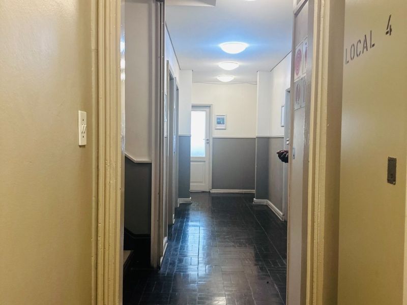 A functional office hallway featuring dark parquet flooring, neutral wall paint with wainscoting, and multiple ceiling light fixtures.