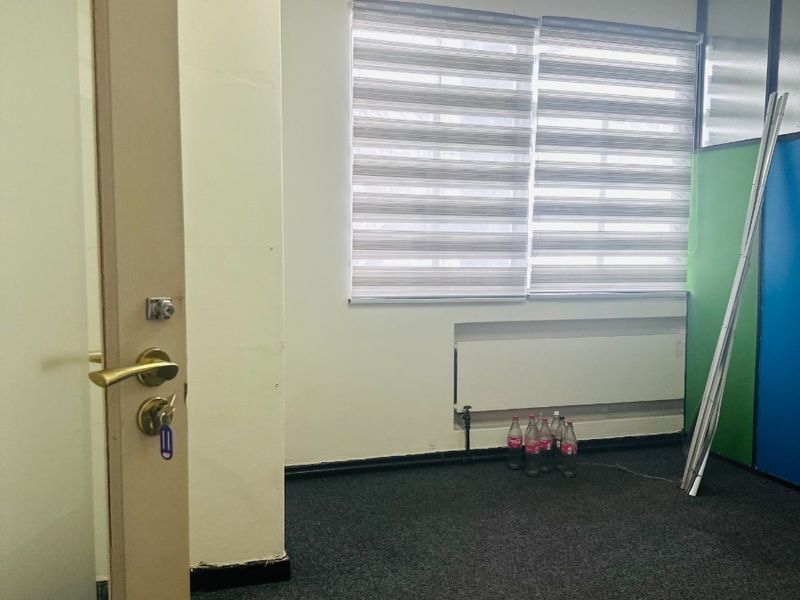 A vacant office space featuring carpet flooring, a radiator, zebra blinds, and a glass partition wall.