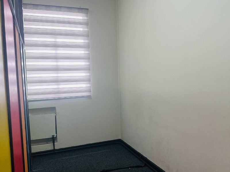 A small, empty office space featuring carpet flooring, a radiator, and zebra blinds on the window.
