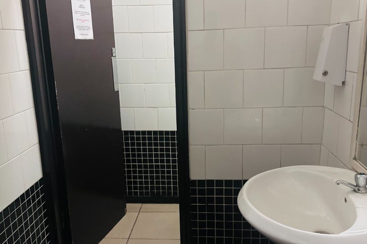 A functional office bathroom featuring a pedestal basin, wall-mounted soap dispenser, and classic black and white tiled finishes.