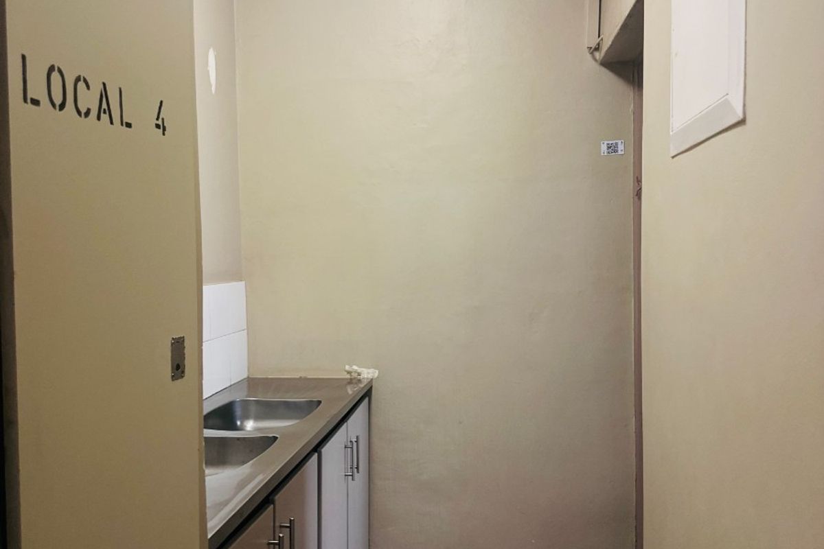 A compact office kitchenette featuring built-in cabinetry, a stainless steel sink, and tiled flooring.