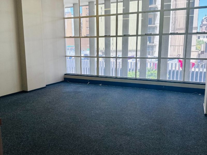 A bright, empty office space featuring large grid-pattern windows, neutral walls, and carpeted flooring, suitable for a professional workspace.