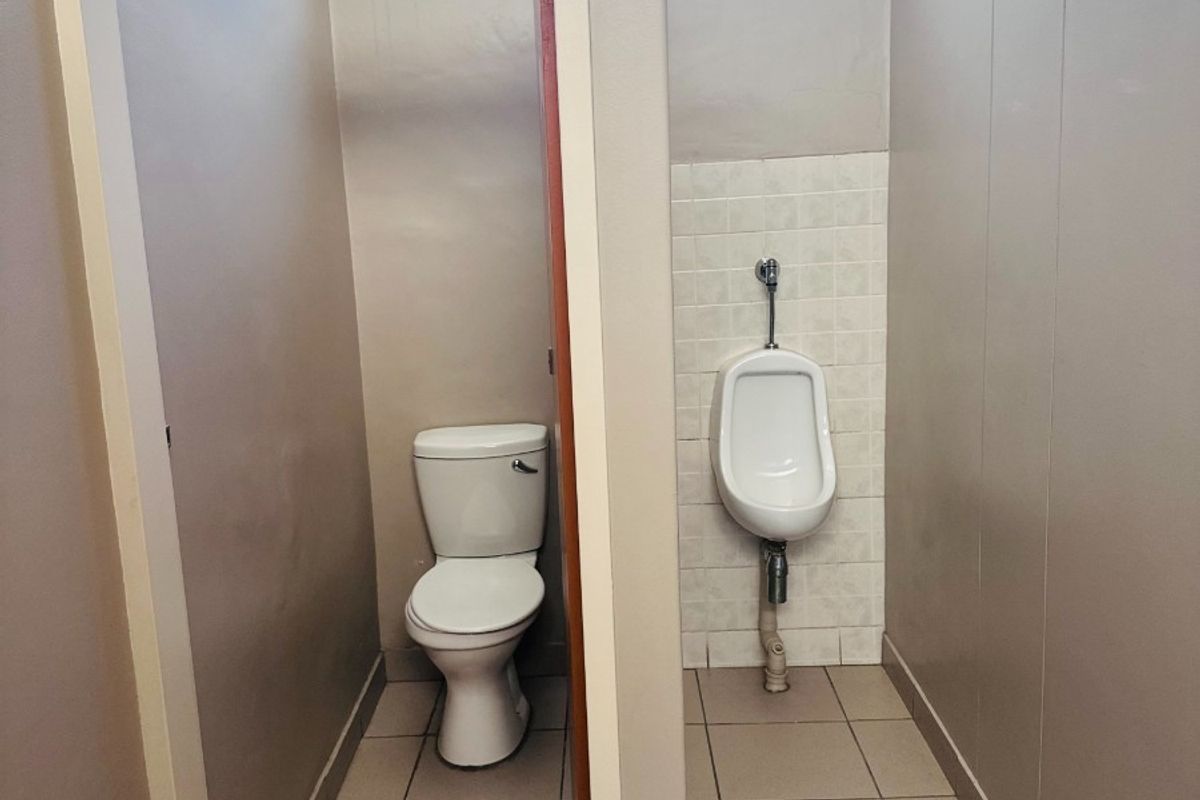 A functional office restroom featuring a standard toilet and wall-mounted urinal with tiled flooring and splashback.