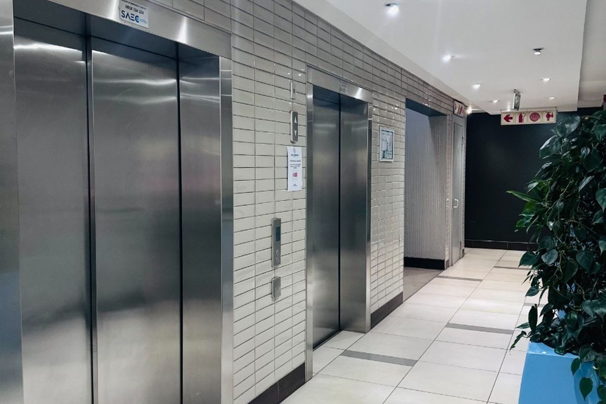 A clean, modern office building hallway featuring stainless steel elevator banks, tiled flooring, and recessed ceiling lighting.
