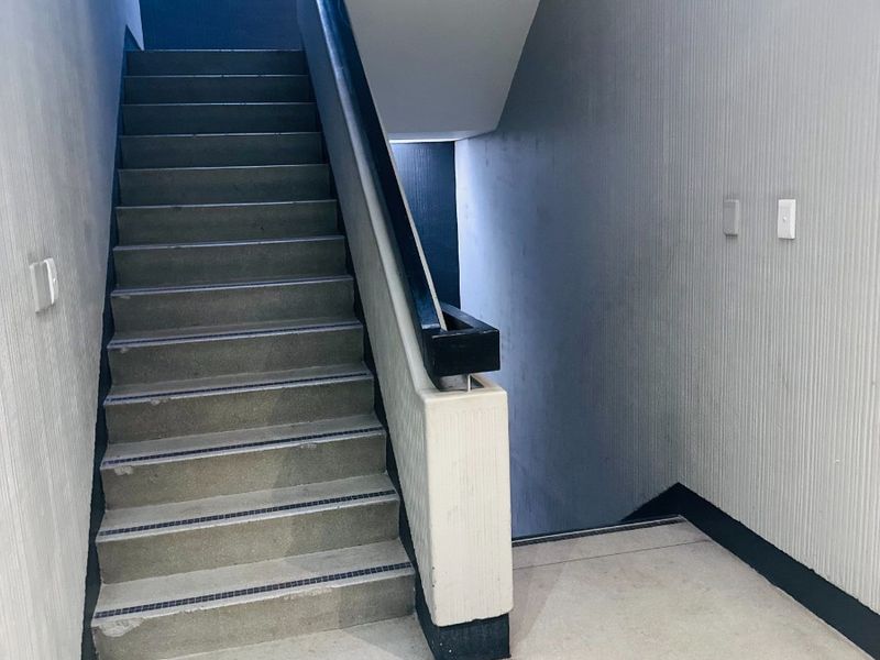 A functional office stairwell featuring concrete steps, a sturdy handrail, and textured wall finishes, providing access between building levels.