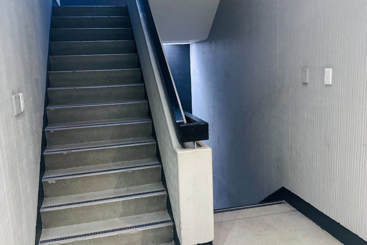 A functional office stairwell featuring concrete steps, a sturdy handrail, and textured wall finishes, providing access between building levels.