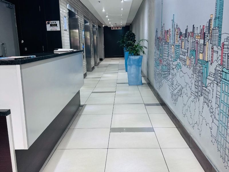 A modern office building entrance lobby featuring a reception desk, tiled flooring, recessed lighting, and elevator access.