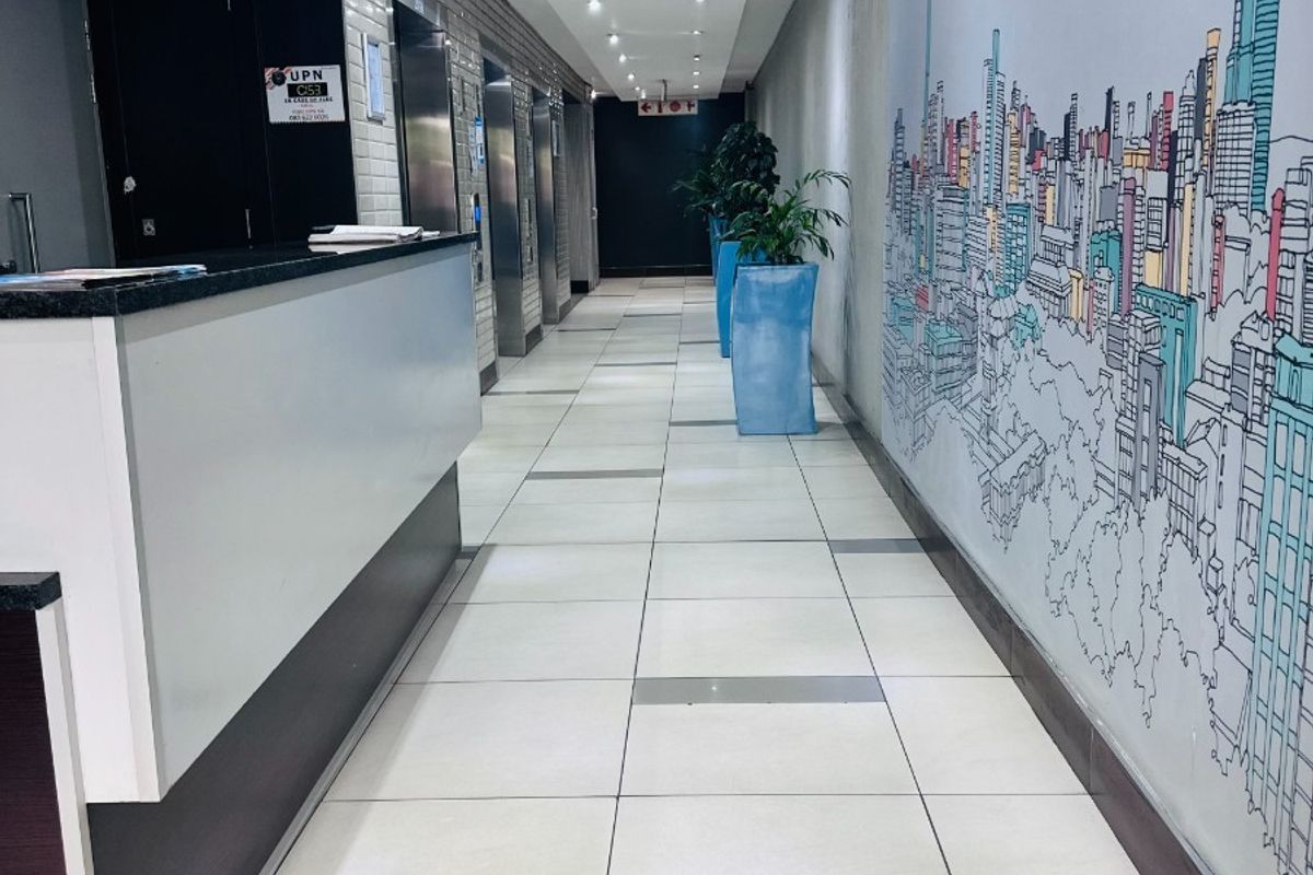 A modern office building entrance lobby featuring a reception desk, tiled flooring, recessed lighting, and elevator access.