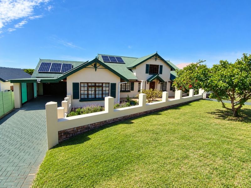 Front elevation of a well-maintained house featuring a paved driveway, solar panels, and a landscaped front garden with a perimeter boundary wall.