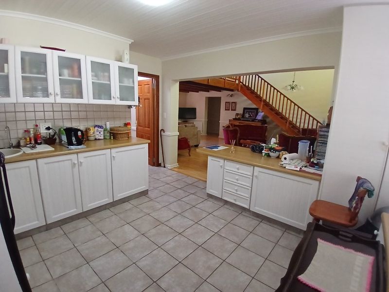 Open plan kitchen featuring white cabinetry and tiled flooring, flowing into a living area with a prominent wooden staircase.