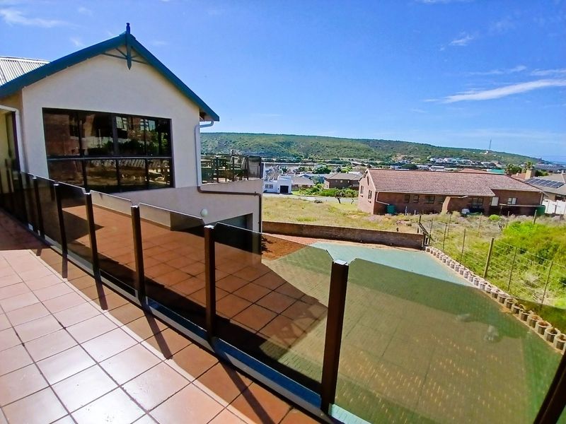Spacious elevated balcony featuring tiled flooring and a modern glass balustrade, offering expansive views of the surrounding neighborhood and landscape.
