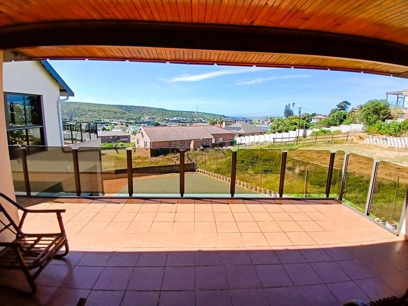 A covered balcony featuring tiled flooring, a glass balustrade, and a timber ceiling, offering expansive views of the surrounding neighborhood and landscape.