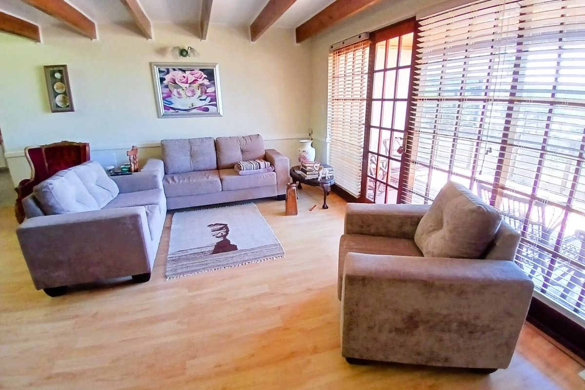 A comfortable living room featuring exposed timber ceiling beams, light laminate flooring, and large french doors with venetian blinds providing natural light.