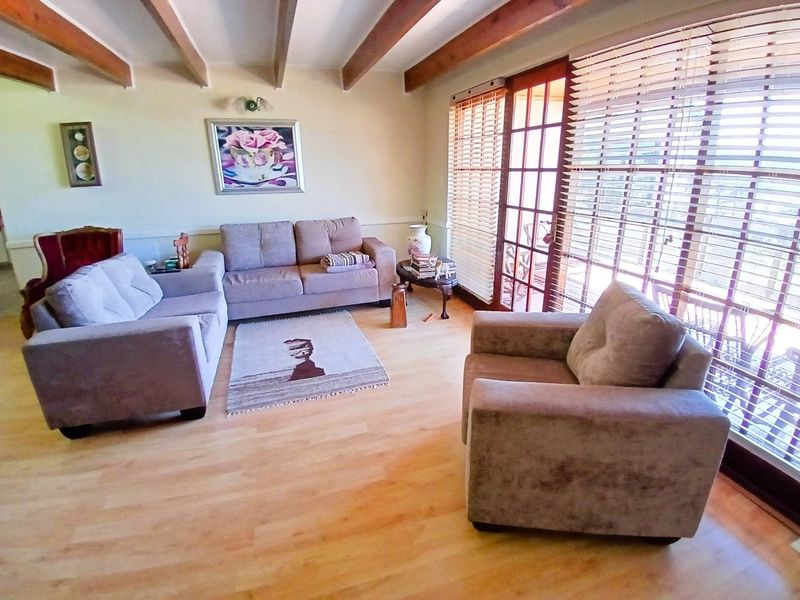 A comfortable living room featuring exposed timber ceiling beams, light laminate flooring, and large french doors with venetian blinds providing natural light.