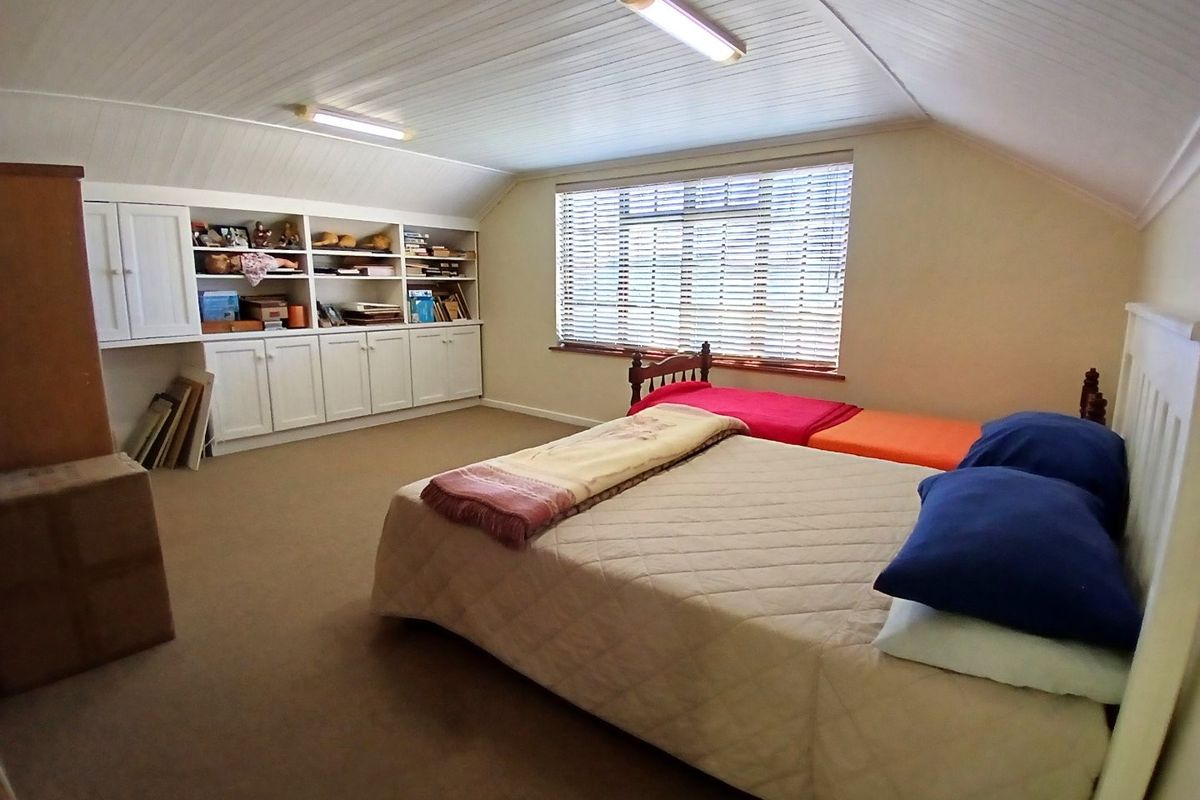 Spacious bedroom featuring built-in cabinetry, sloped ceilings, and large windows with venetian blinds, offering ample storage and natural light.