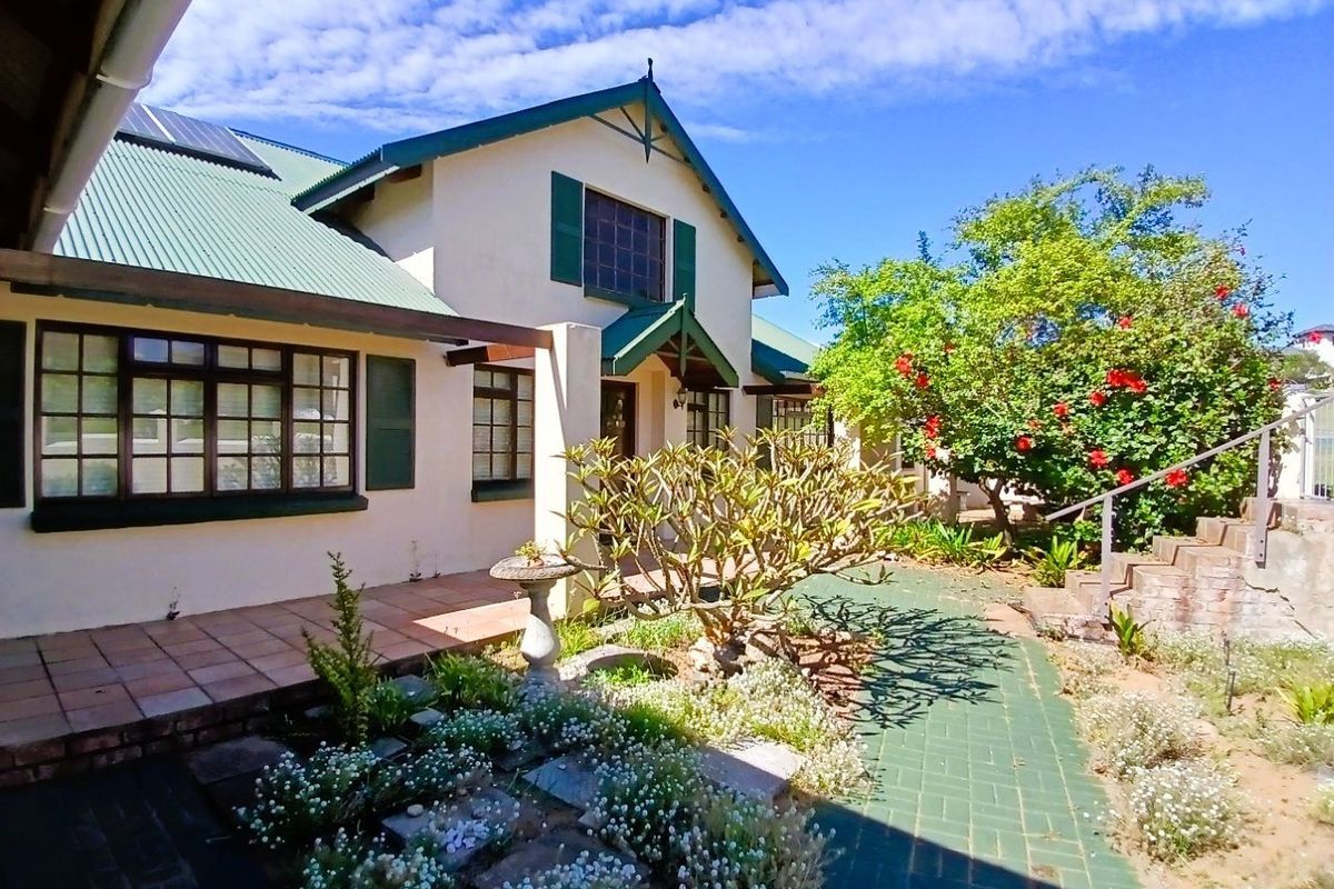 A well-maintained rear exterior view featuring a tiled patio, brick pathways, established garden, and a pitched roof with integrated solar panels.