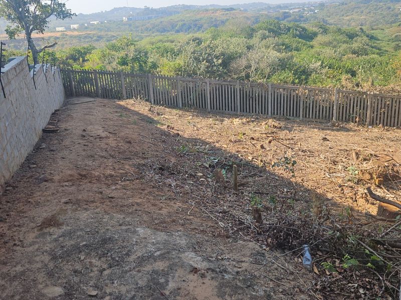 A vacant residential plot featuring a concrete block boundary wall with electric fencing and a rear picket-style fence overlooking a natural landscape.
