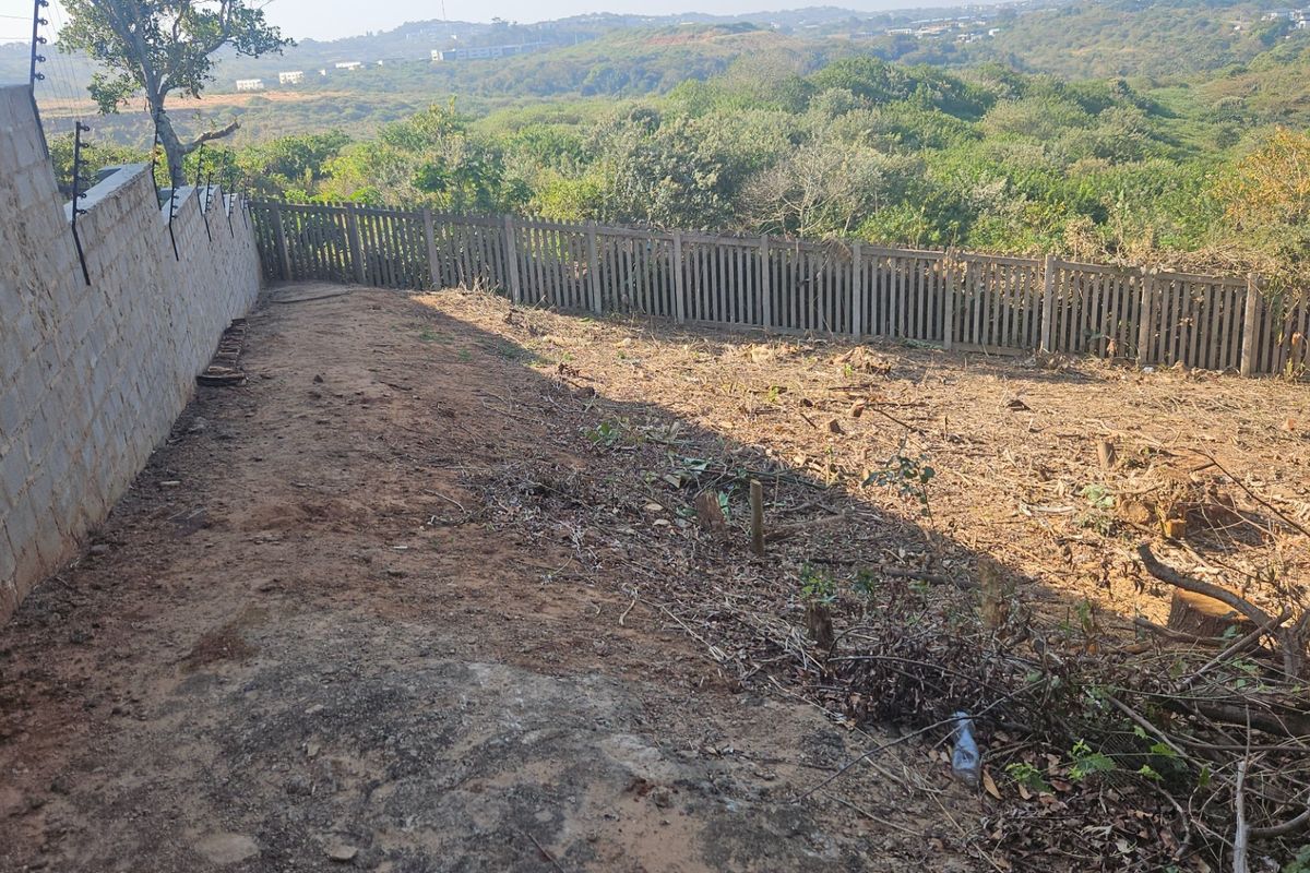 A vacant residential plot featuring a concrete block boundary wall with electric fencing and a rear picket-style fence overlooking a natural landscape.