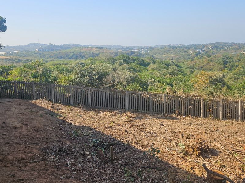A vacant residential plot featuring a perimeter fence and retaining wall, offering expansive views of the surrounding natural landscape.