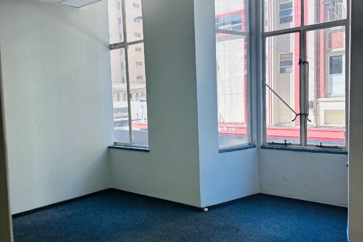 A vacant, well-lit office space featuring large windows, carpeted flooring, and a suspended ceiling with recessed lighting.