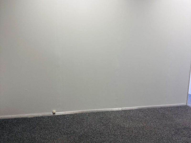 A vacant office space featuring neutral wall finishes, grey carpet flooring, and a suspended ceiling, providing a clean and functional work environment.