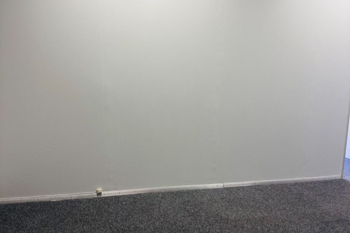 A vacant office space featuring neutral wall finishes, grey carpet flooring, and a suspended ceiling, providing a clean and functional work environment.
