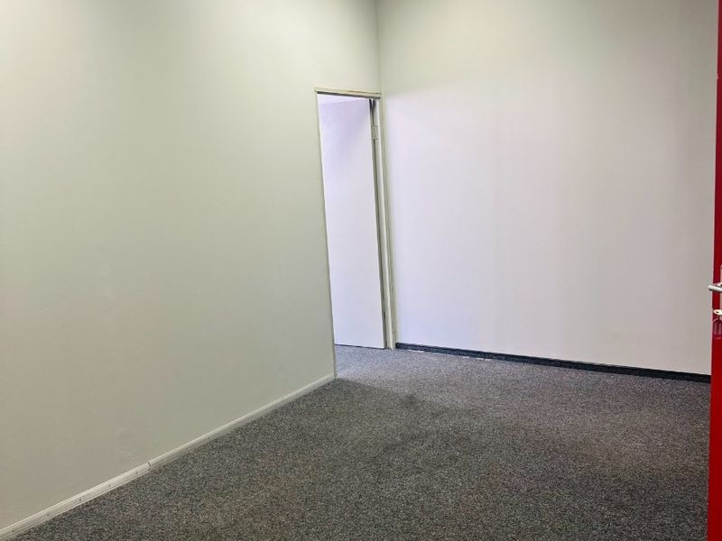 A vacant office space featuring neutral walls, grey carpeting, and a suspended ceiling with integrated recessed lighting.