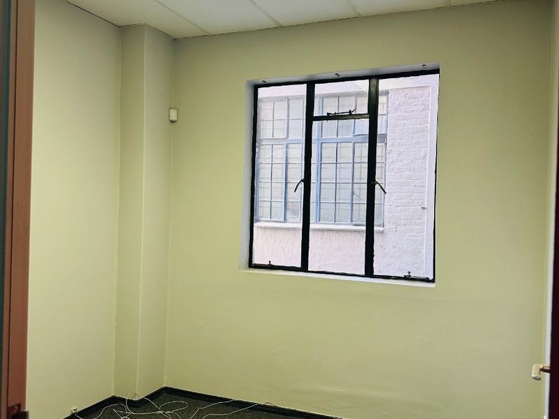 A vacant office space featuring a suspended ceiling with recessed lighting, carpeted flooring, and a metal-framed window providing natural light.