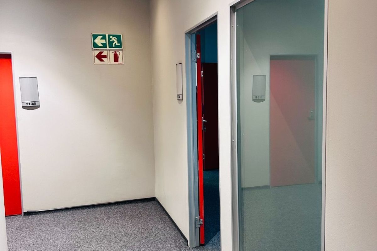 A clean office hallway featuring carpeted flooring, a suspended ceiling with recessed lighting, and glass partitioning between office spaces.