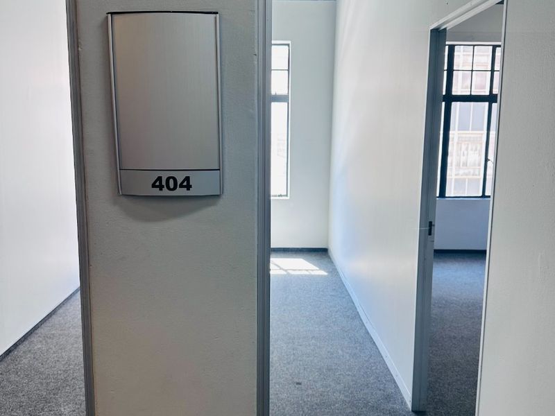 A vacant office space featuring neutral walls, carpeted flooring, and large windows providing natural light, suitable for a professional workspace.