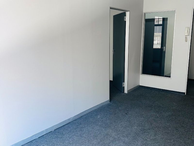 A clean, empty office space featuring grey carpet flooring, an internal glass partition, and a wall-mounted intercom system.