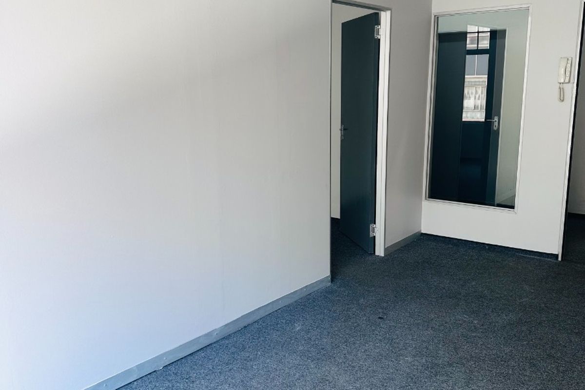 A clean, empty office space featuring grey carpet flooring, an internal glass partition, and a wall-mounted intercom system.