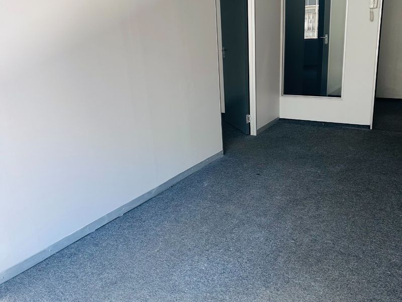 A clean, empty office space featuring grey carpet flooring, an internal glass partition, and a wall-mounted intercom system.