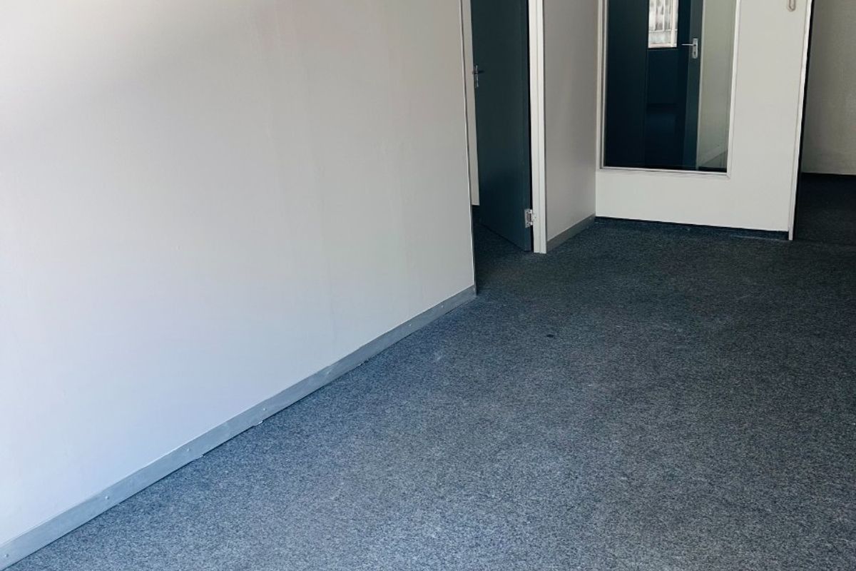A clean, empty office space featuring grey carpet flooring, an internal glass partition, and a wall-mounted intercom system.