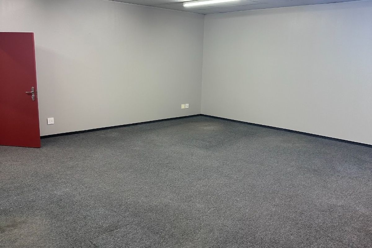 A clean, empty office space featuring neutral grey walls, grey carpeting, and a suspended ceiling with integrated fluorescent lighting.