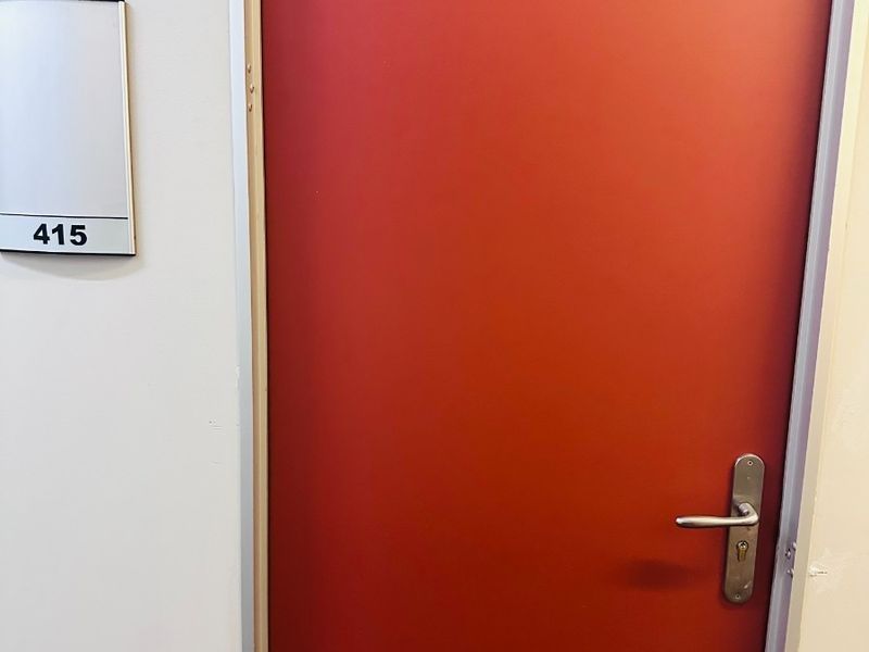 A clean office hallway entrance featuring a red door with a room number sign.