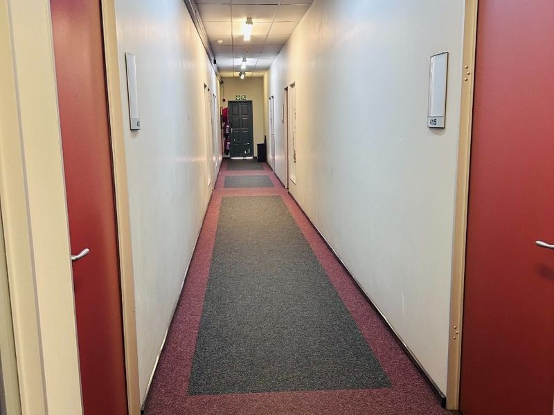 A functional office building hallway featuring a suspended ceiling, fluorescent lighting, and red doors leading to individual office suites.