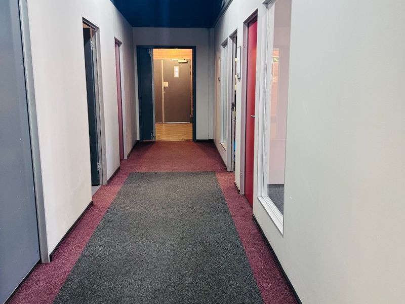 A functional office hallway featuring carpeted flooring, multiple access doors, and internal glass partitions, providing a clean and professional circulation space.