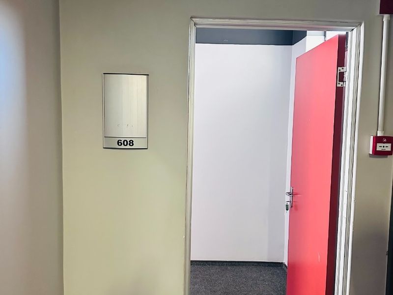 An empty office space featuring carpeted flooring, a red door, and integrated fire safety infrastructure.