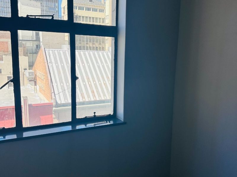 An empty office space featuring a large metal-framed window with an urban city view.