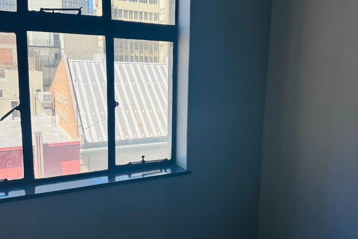 An empty office space featuring a large metal-framed window with an urban city view.