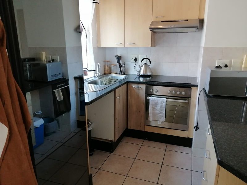 Compact kitchen featuring laminate cabinetry, granite countertops, built-in oven with extractor fan, and tiled flooring.