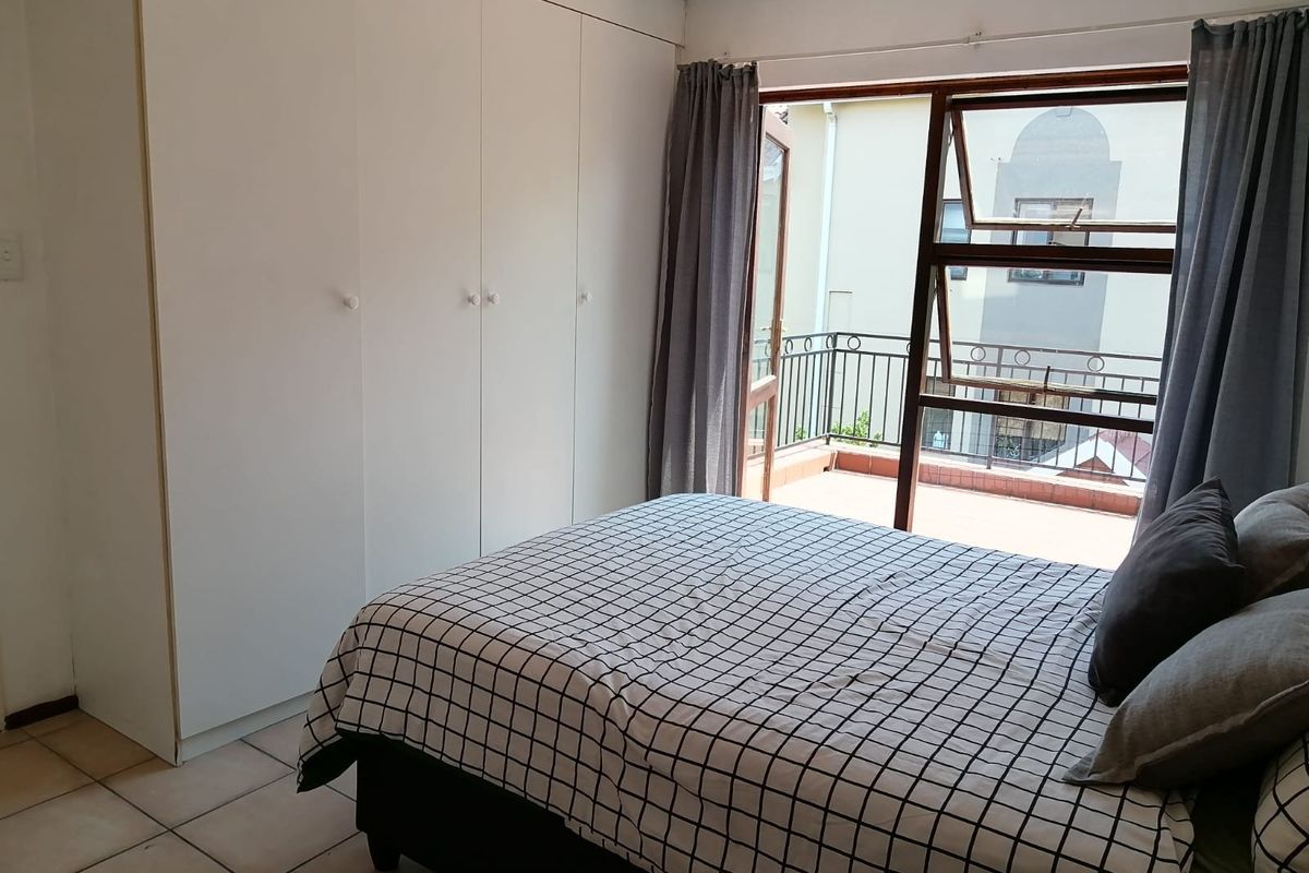 A bedroom featuring built-in cupboards, tiled flooring, and direct access to a private balcony through a timber-framed door.