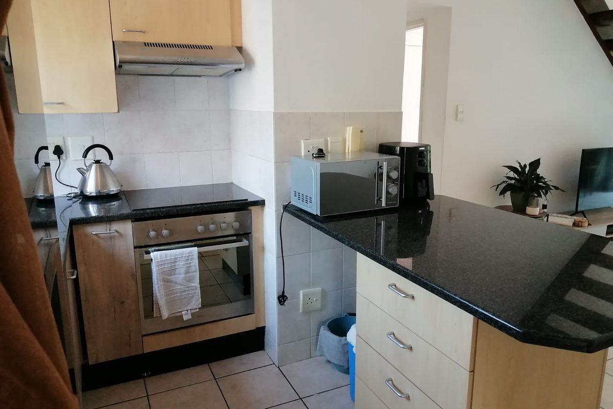 Compact kitchen featuring light wood cabinetry, granite countertops, built-in oven, electric hob, and tiled flooring, offering a functional layout for daily use.
