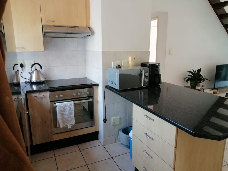 Compact kitchen featuring light wood cabinetry, granite countertops, built-in oven, electric hob, and tiled flooring, offering a functional layout for daily use.