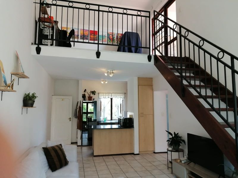 Open plan living area featuring a mezzanine level with wrought iron balustrades, a wooden staircase, and a functional kitchen with built-in cabinetry.